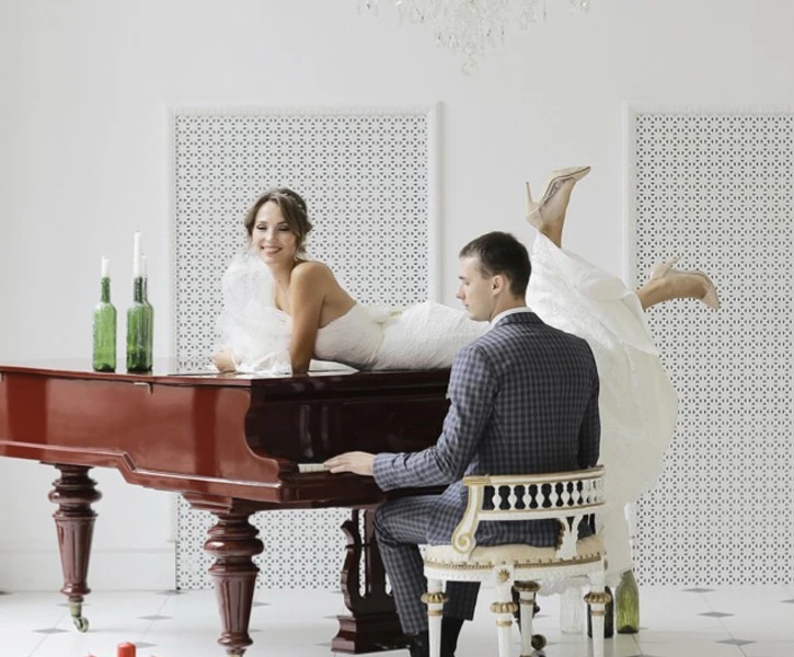 ピアノの上で微笑むウェディングドレス姿の新婦と、演奏する新郎