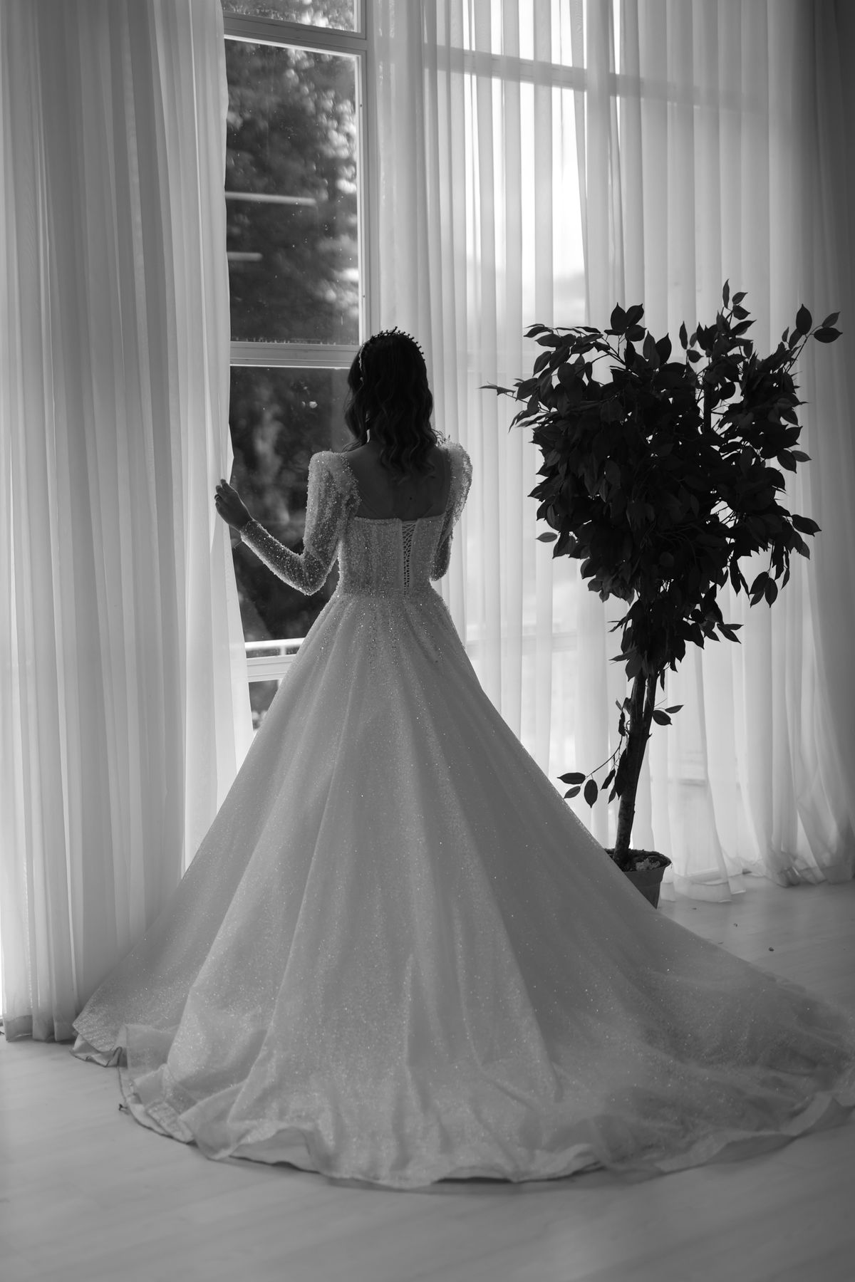 窓辺に立つウェディングドレス姿の新婦を写したモノクロ写真